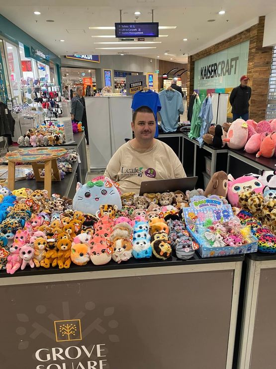 A man is sitting in front of a table full of stuffed animals.