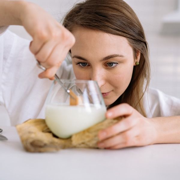 A woman is pouring candle wax into a glass with a wick.