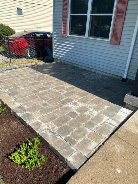 A brick walkway leading to a house with a red car parked in front of it.