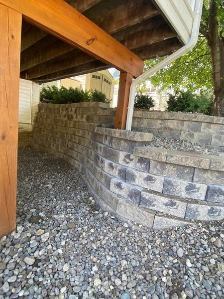 A brick wall under a wooden deck with a tree in the background.