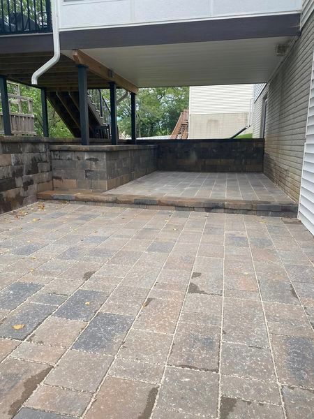 A patio with a deck underneath it and a house in the background.