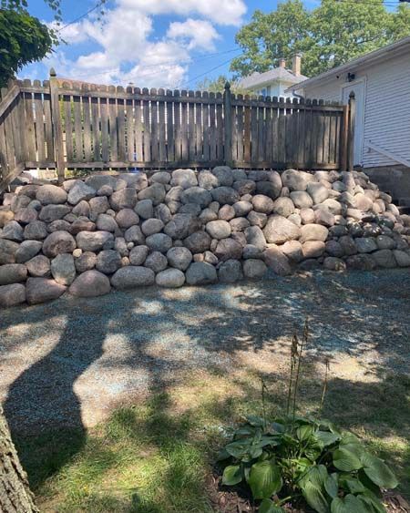 A large rock wall in a backyard next to a wooden fence.