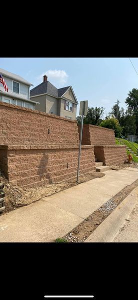 A brick wall is being built next to a sidewalk and a house.