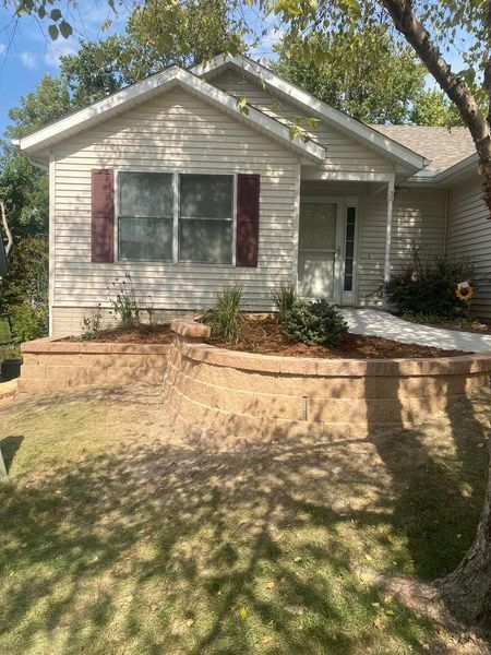 A small white house with a stone wall in front of it.