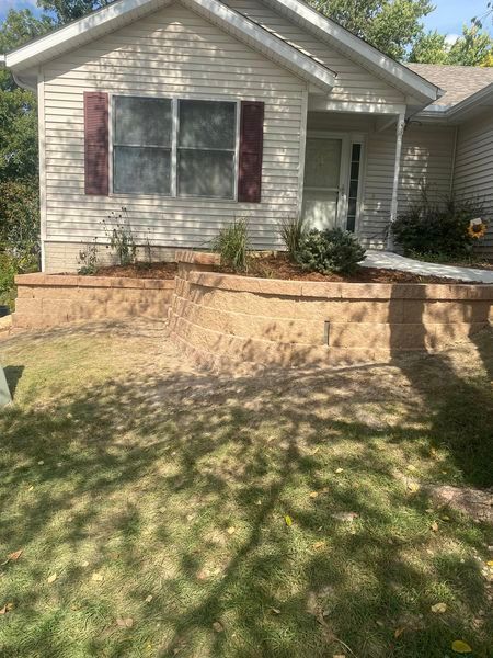 A small white house with a stone wall in front of it.