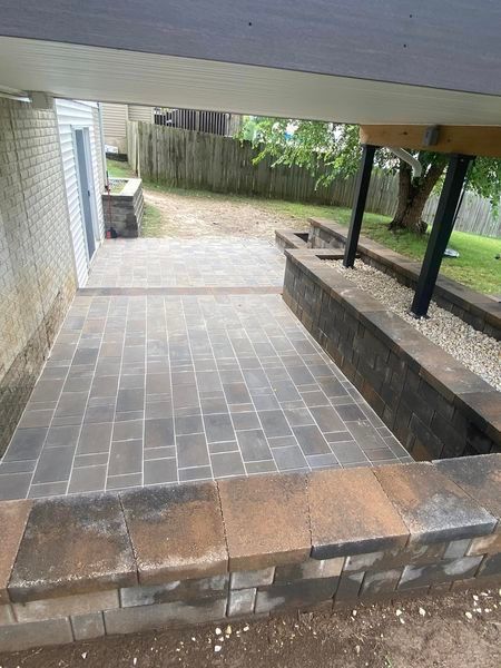 A patio with a stone wall and steps under a house.