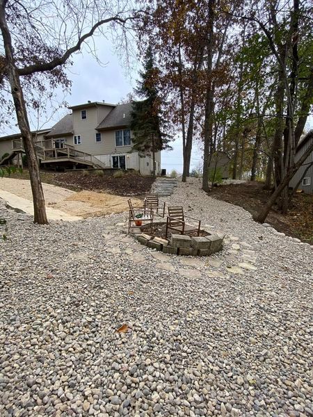A fire pit is in the middle of a gravel driveway in front of a house.