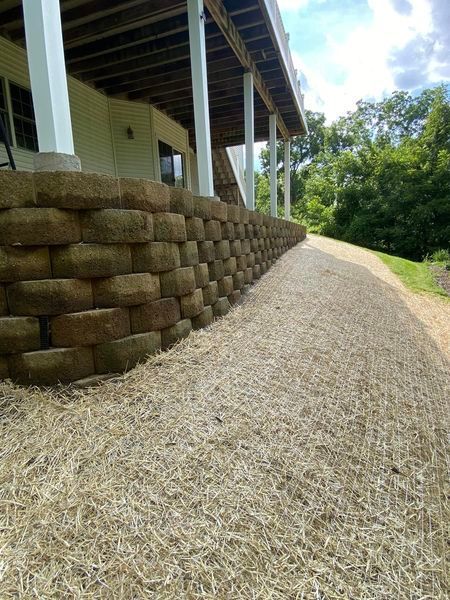 A stone retaining wall along a dirt path in front of a house.