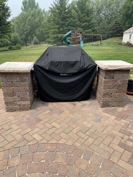 A grill with a black cover is sitting on a brick patio