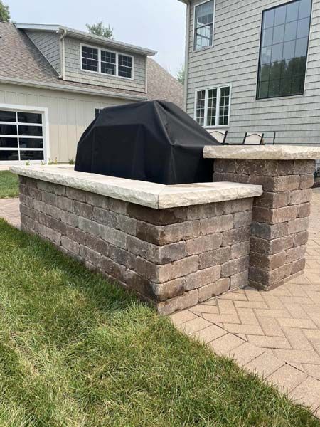 A grill is sitting on top of a brick wall next to a house.
