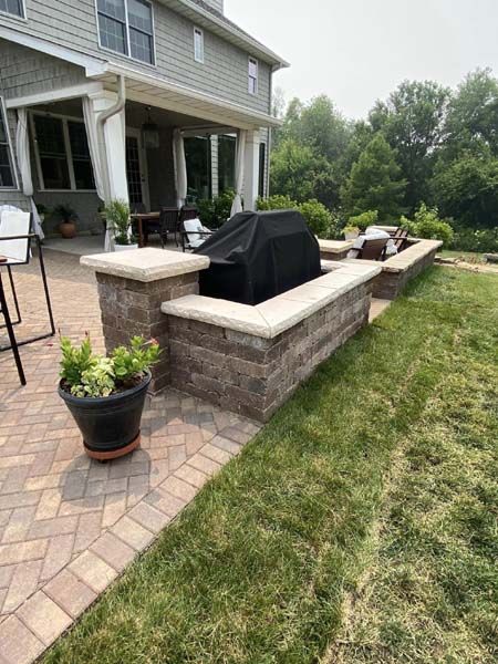 A patio with a grill and a potted plant in front of a house.