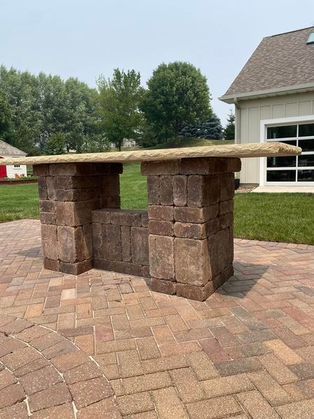 A wooden table is sitting on a brick patio in front of a house.
