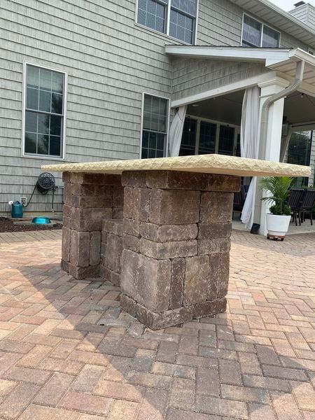 A table made of bricks is sitting on a brick patio in front of a house.