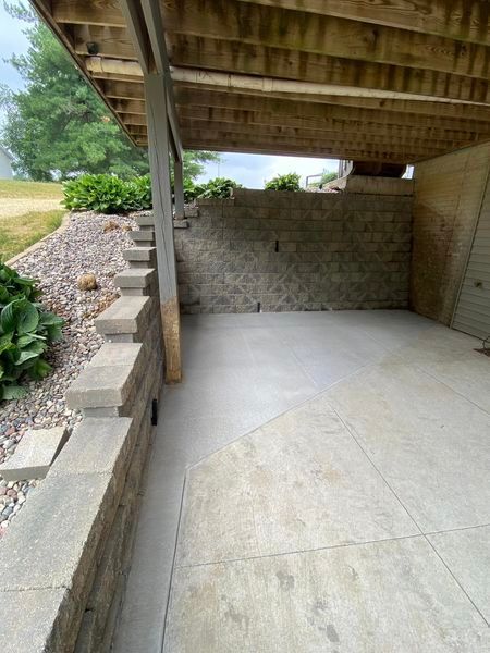 A concrete patio under a wooden deck with stairs leading up to it.
