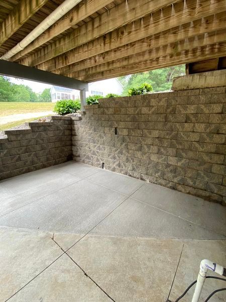 A concrete patio under a wooden deck with a brick wall.