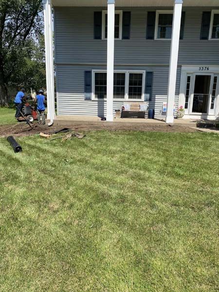 A group of people are working on a lawn in front of a house.