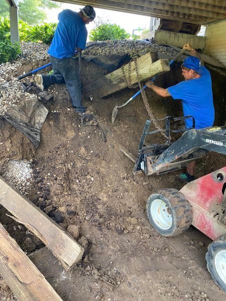 Two men are digging in the dirt under a bridge.