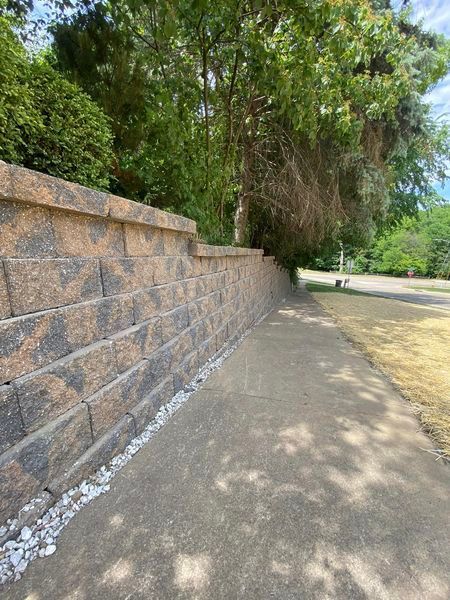A brick wall along a sidewalk with trees in the background.