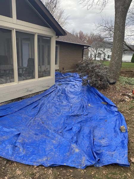 A blue tarp is laying on the ground in front of a house.