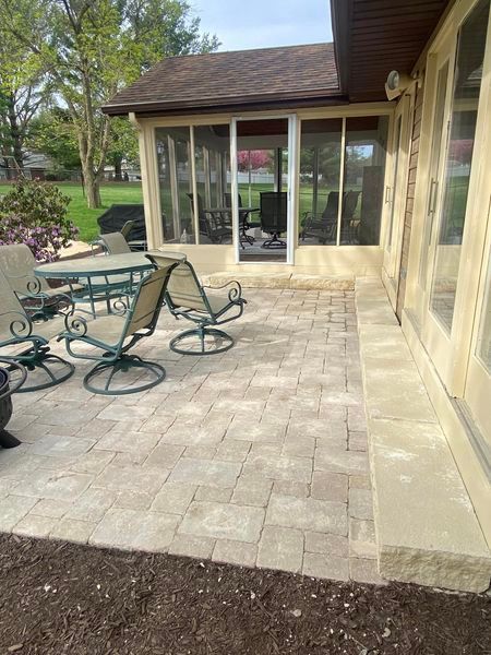 A patio with a table and chairs in front of a screened in porch.