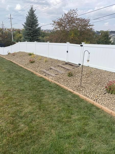 A backyard with a white fence and a lush green lawn.