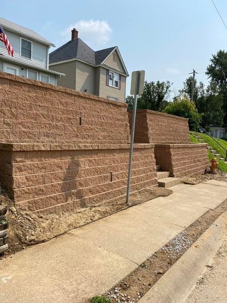 A brick wall is being built next to a sidewalk in front of a house.