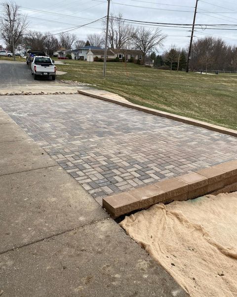 A white truck is parked on the side of the road next to a brick driveway.