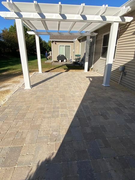A white pergola is sitting on top of a patio next to a house.
