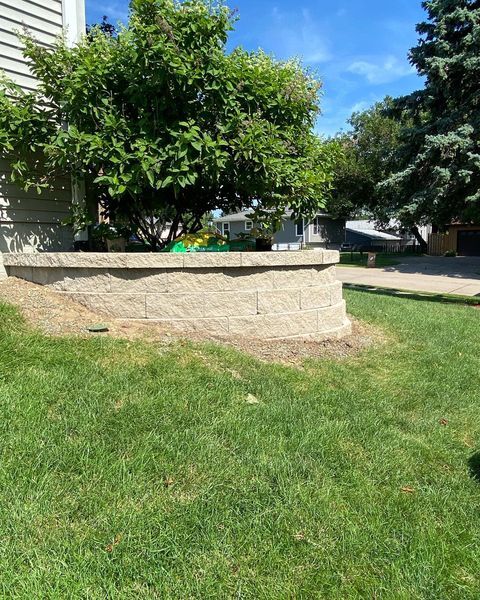 A brick wall is sitting in the middle of a lush green lawn in front of a house.