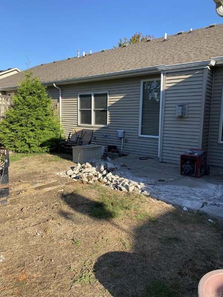 A person is standing in front of a house with a generator in the backyard.