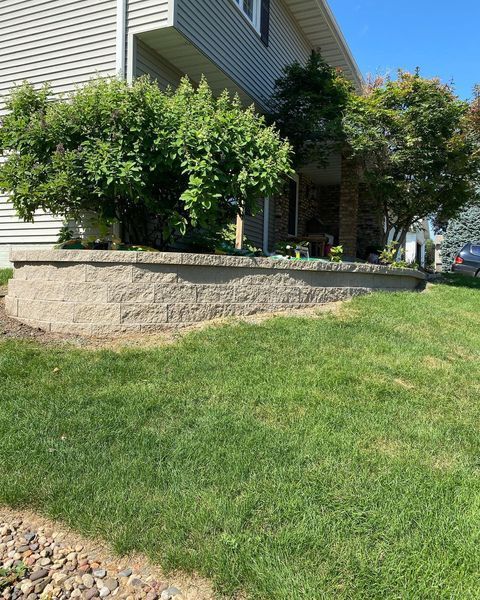 A house with a stone wall in front of it and a lush green lawn.