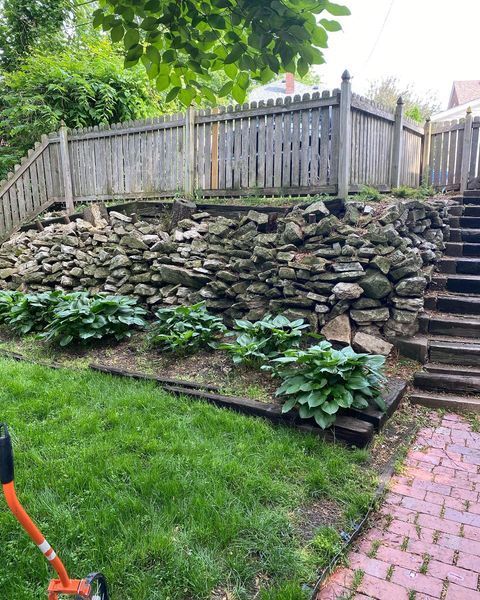A lawn mower is sitting in a yard next to a stone wall and stairs.