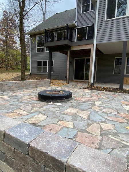 A stone patio with a fire pit in the middle of it in front of a house.