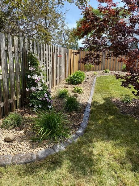 A wooden fence surrounds a lush green yard with flowers and shrubs.