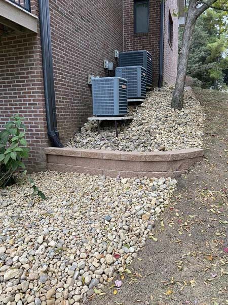 Two air conditioners are sitting on top of a pile of rocks next to a brick building.