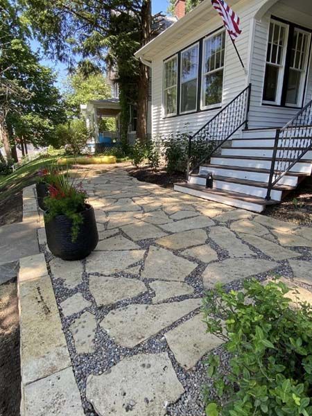 A stone walkway leading to a white house with stairs and a flag.