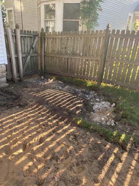 A wooden fence surrounds a muddy yard in front of a house.