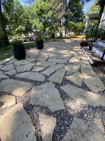 A stone walkway with potted plants on it in front of a house.