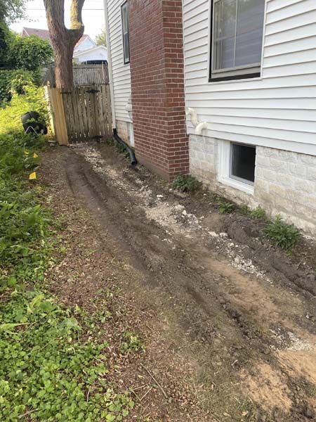 A dirt road leading to a white house with a brick wall.
