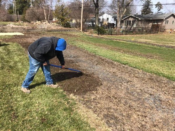 A man is raking the grass on the side of the road.