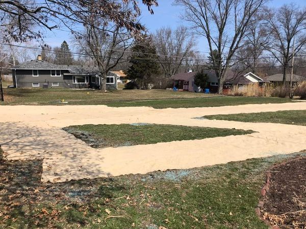A dirt road going through a grassy field with a house in the background.