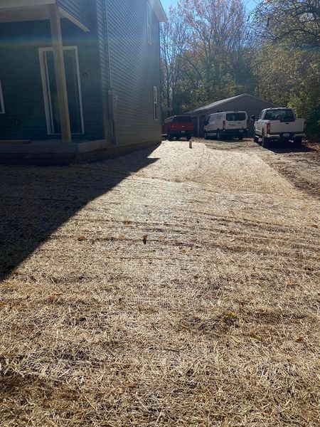 A dirt road leading to a house with cars parked on the side of it.