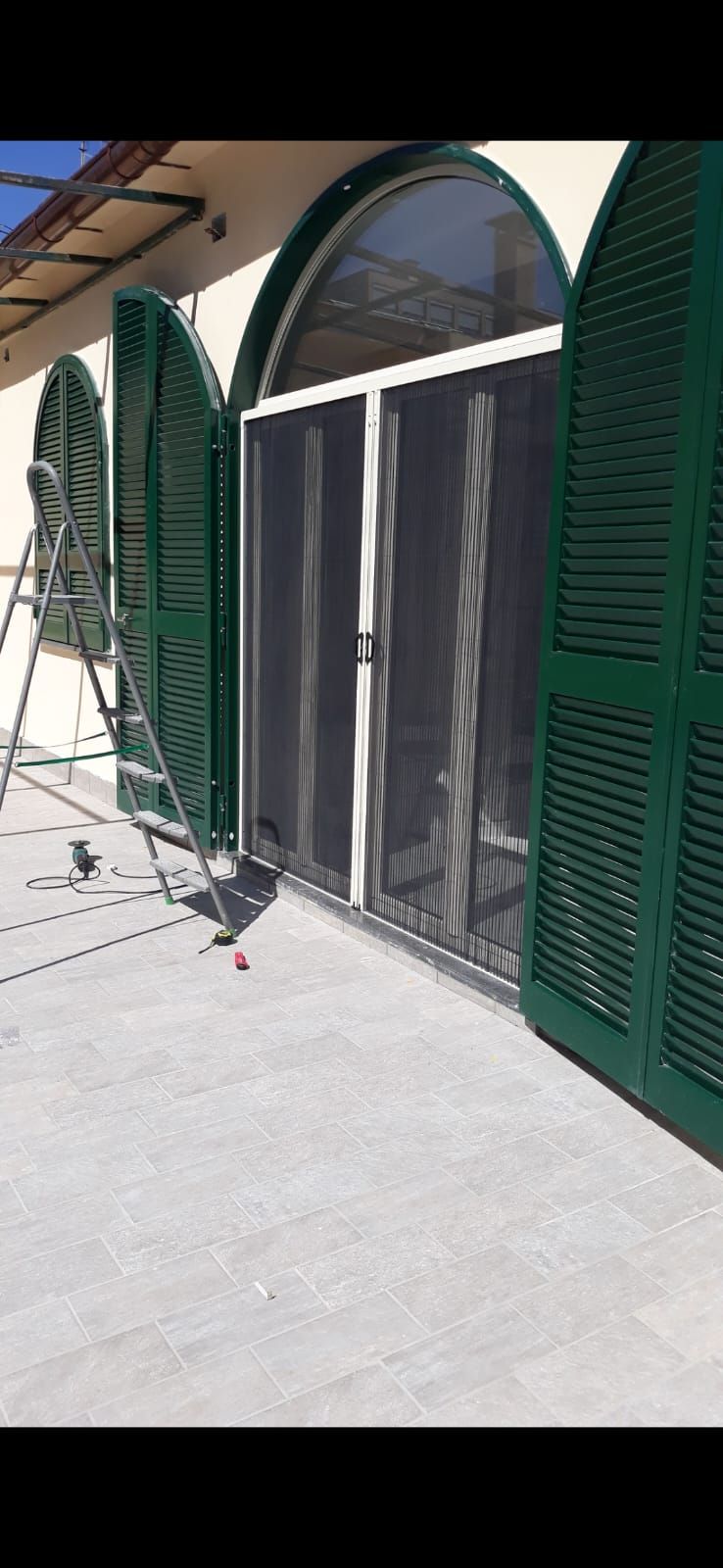 Una porta scorrevole in vetro con persiane verdi sul lato di un edificio.