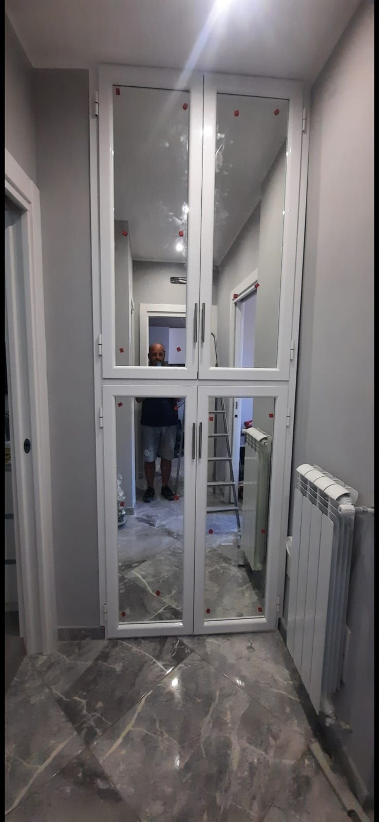 Un corridoio con una porta a specchio e un termosifone.