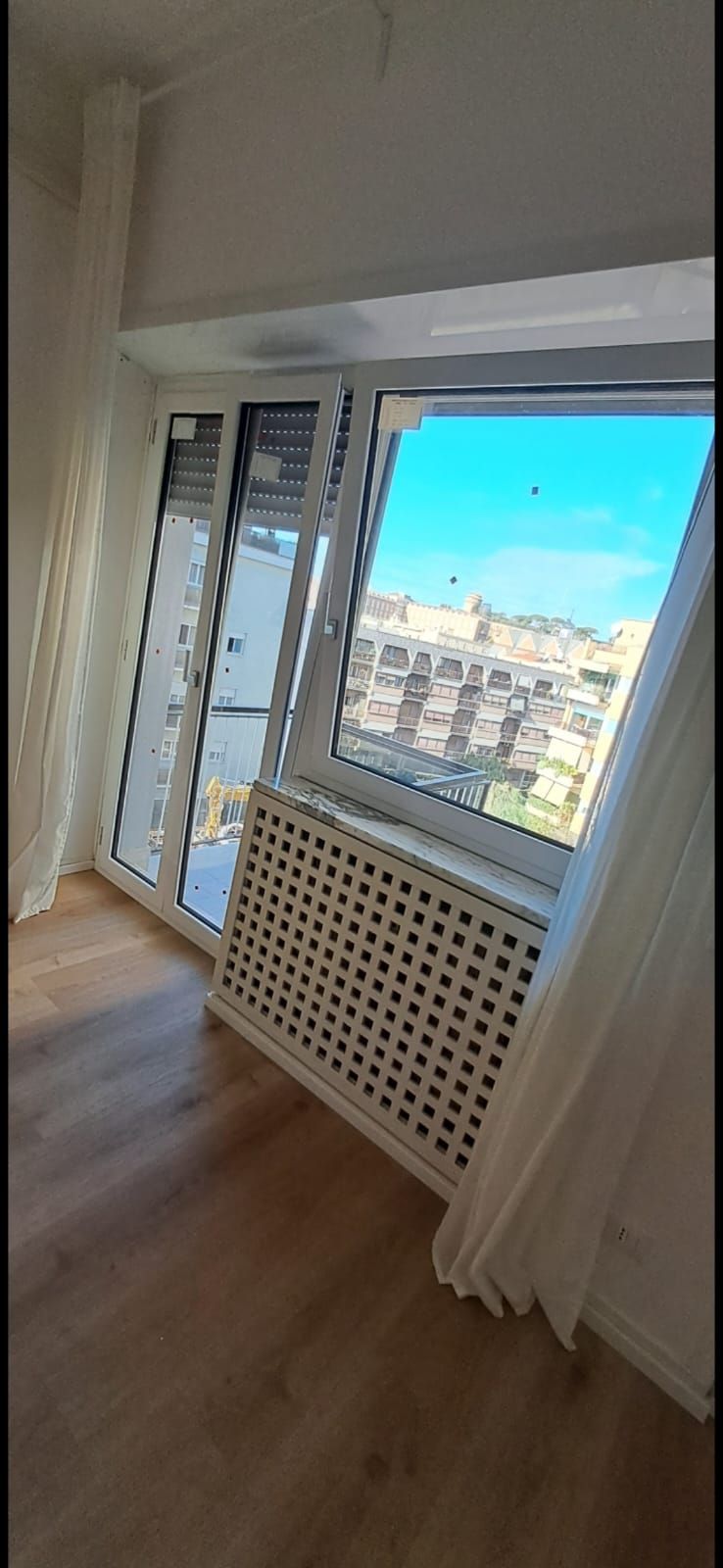 Una stanza vuota con una grande finestra e un termosifone.