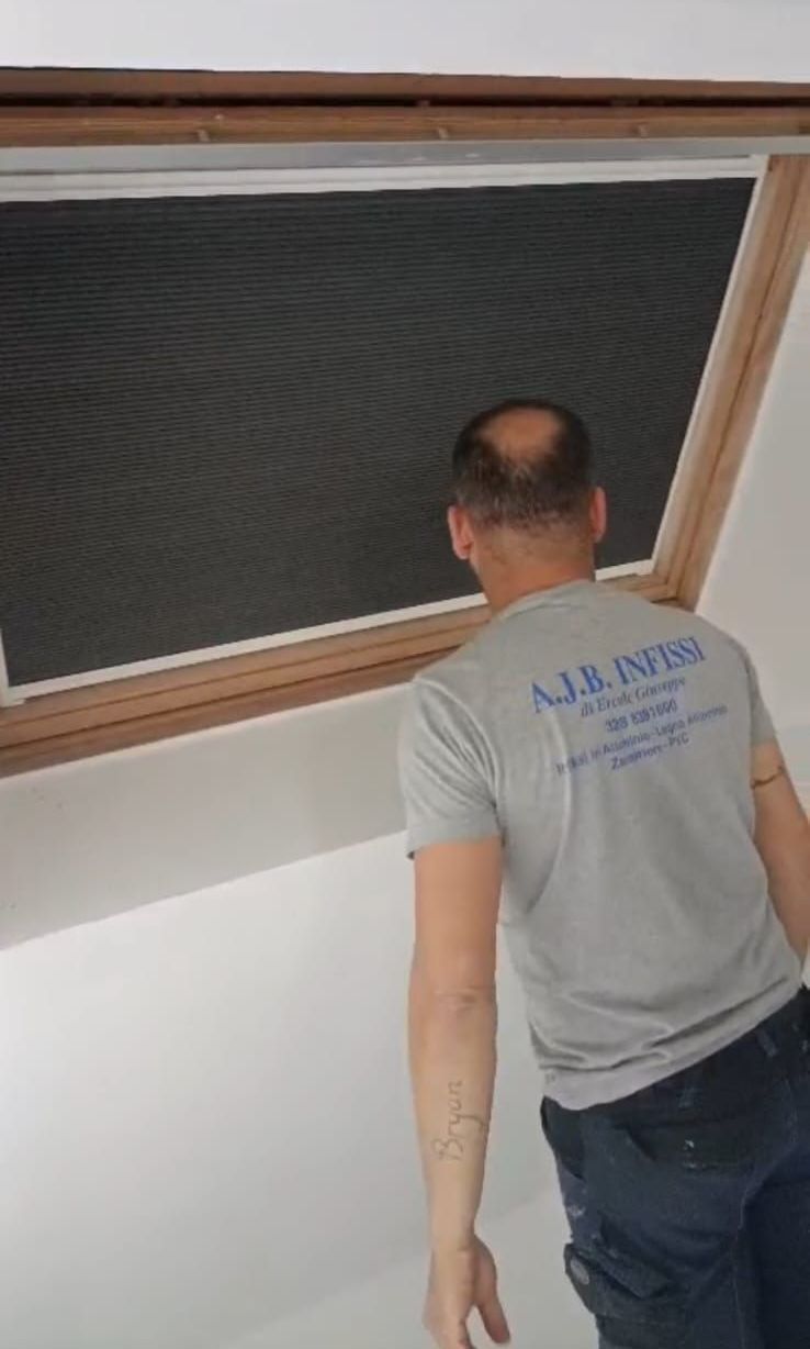 Un uomo con una camicia grigia è in piedi davanti a un lucernario.