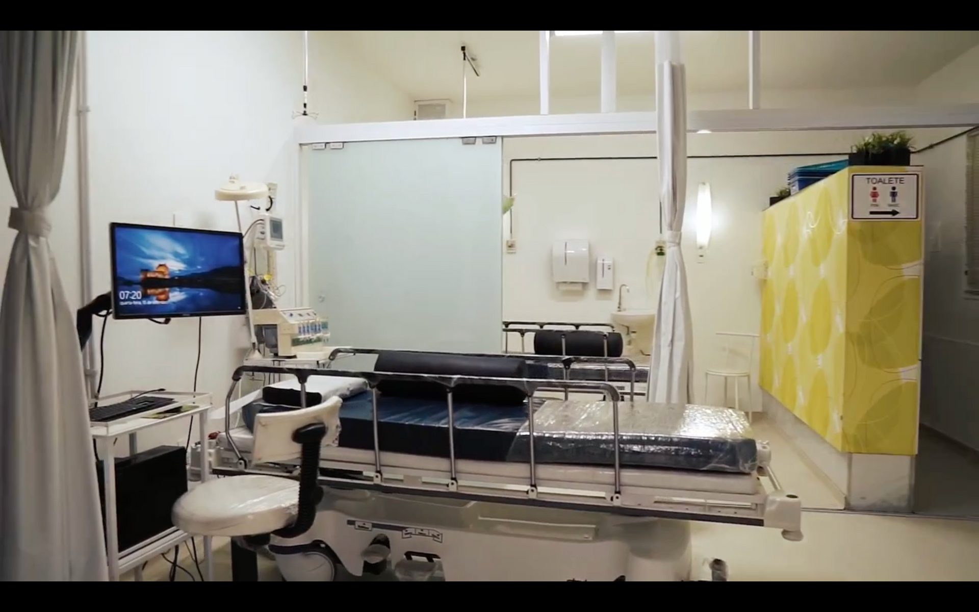 Um quarto de hospital com uma cama, cadeira e televisão.