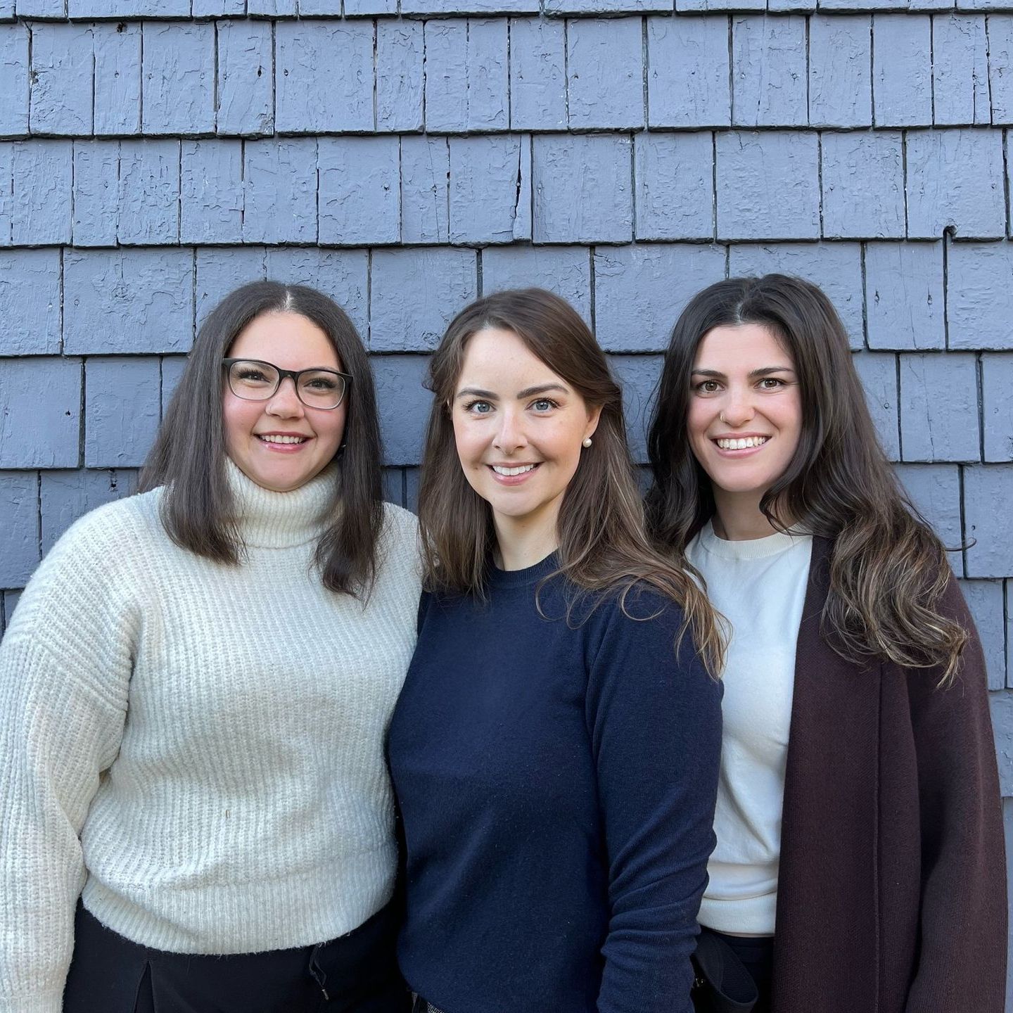 Three women are posing for a picture in front of a blue brick wall