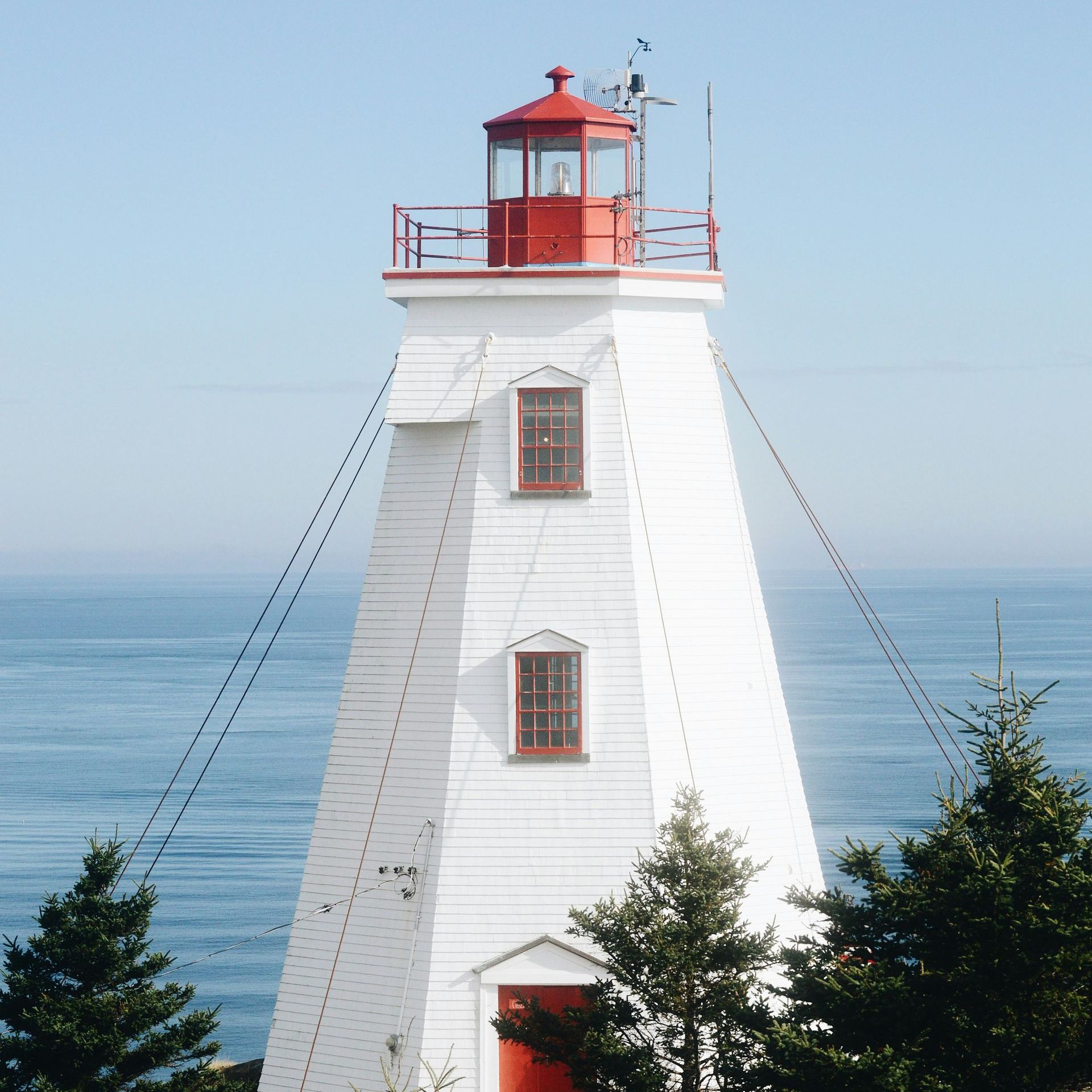 A white lighthouse with a red top stands in front of the ocean