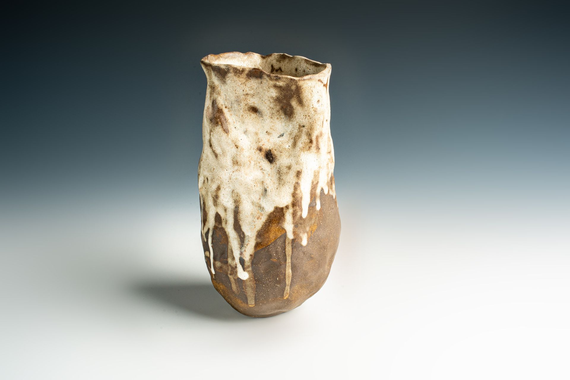 A brown and white vase is sitting on a white surface.